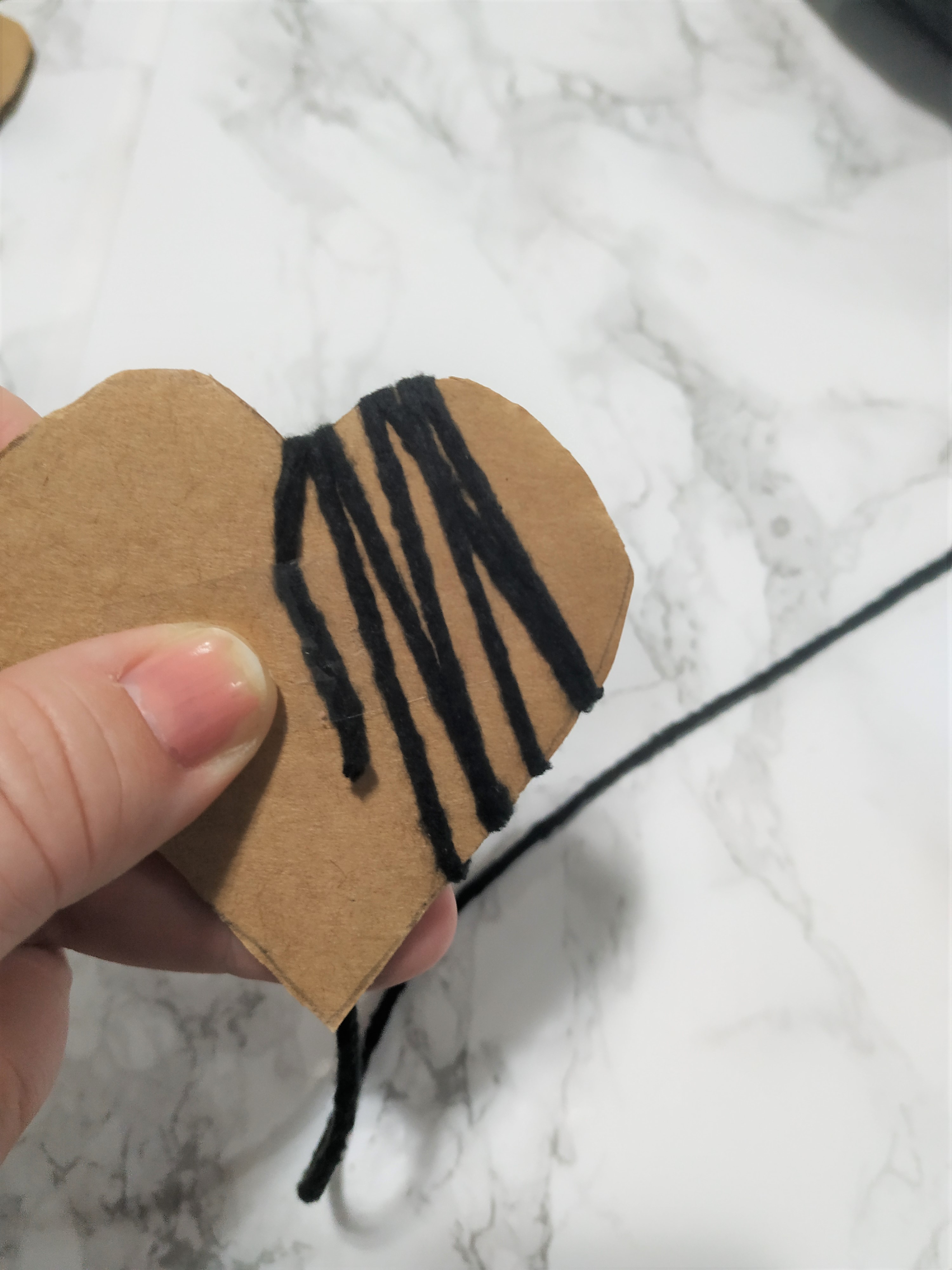 wrapping black yarn around a cardboard heart cut out.