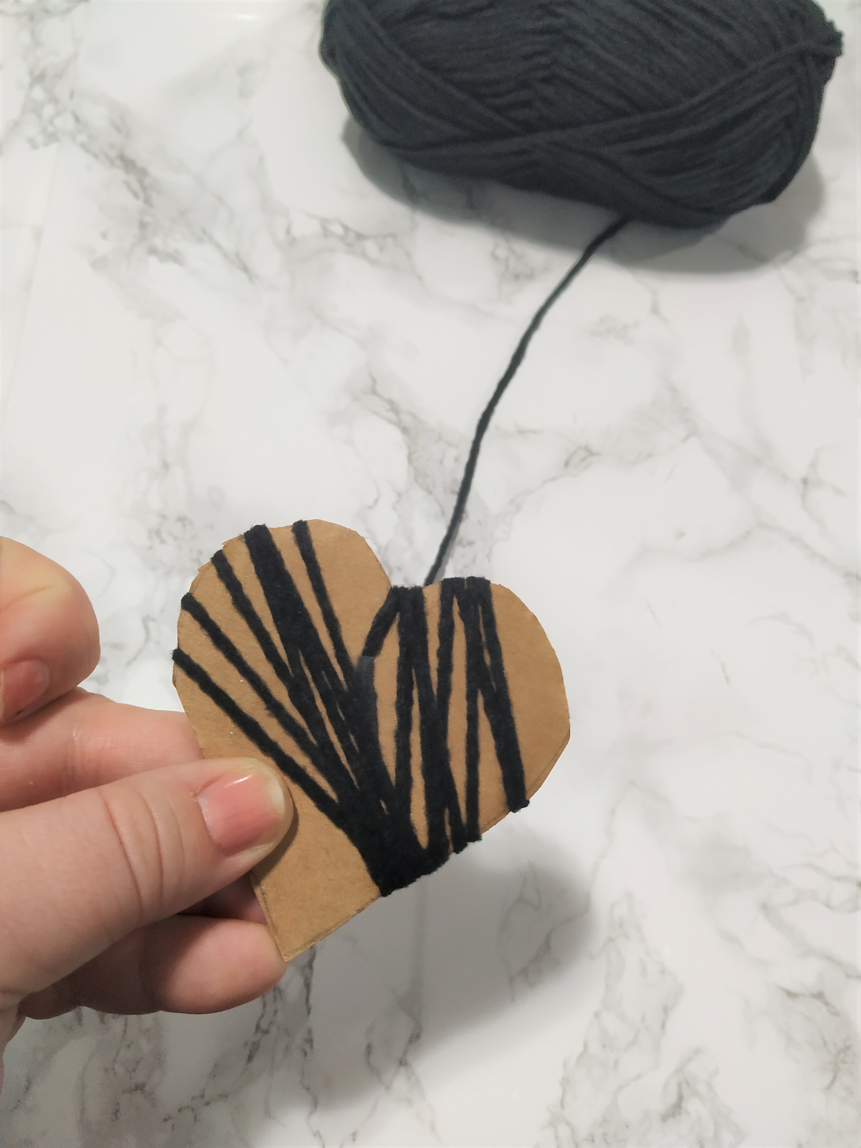 wrapping black yarn around a cardboard heart cut out.
