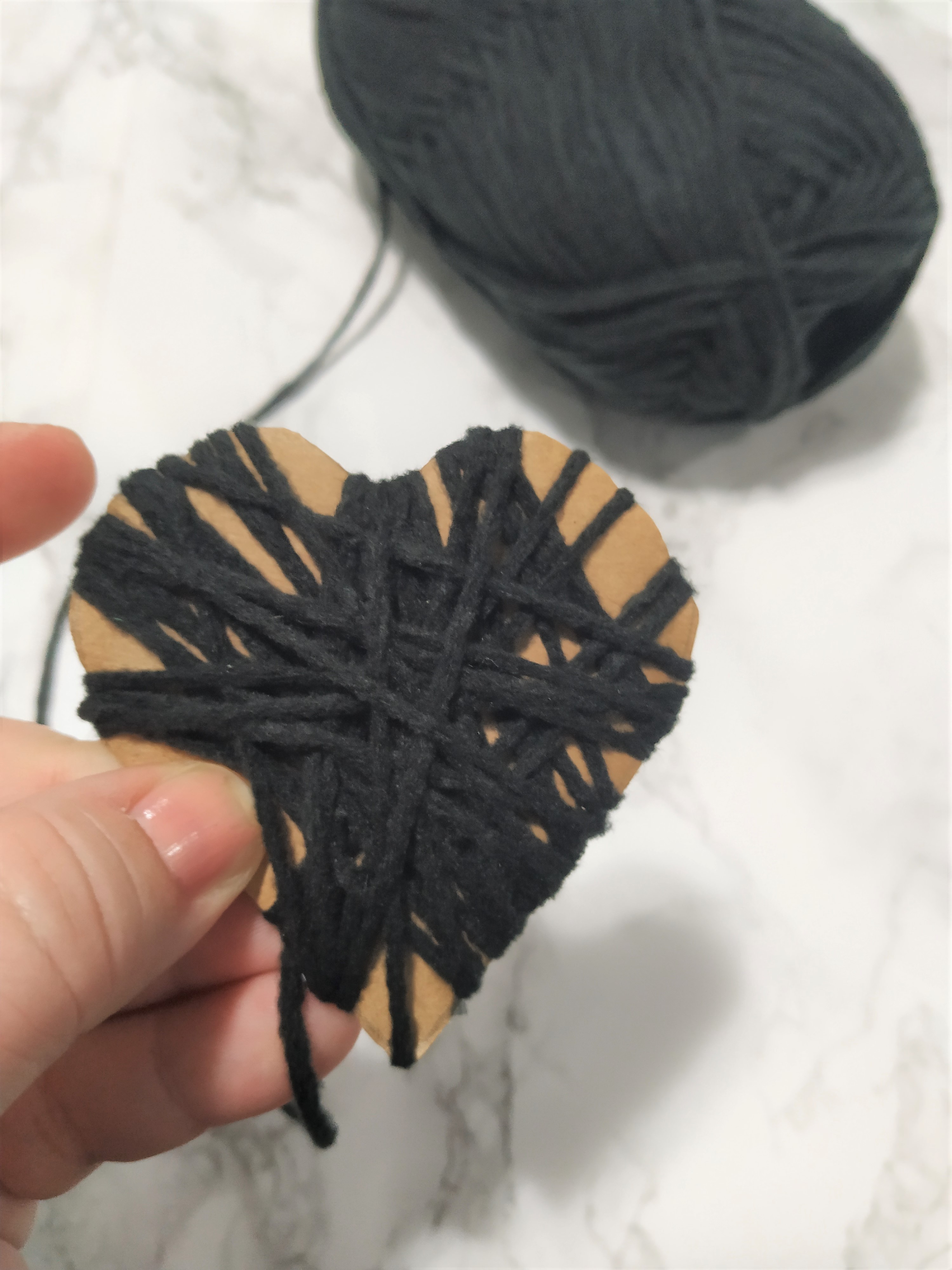wrapping black yarn around a cardboard heart cut out.