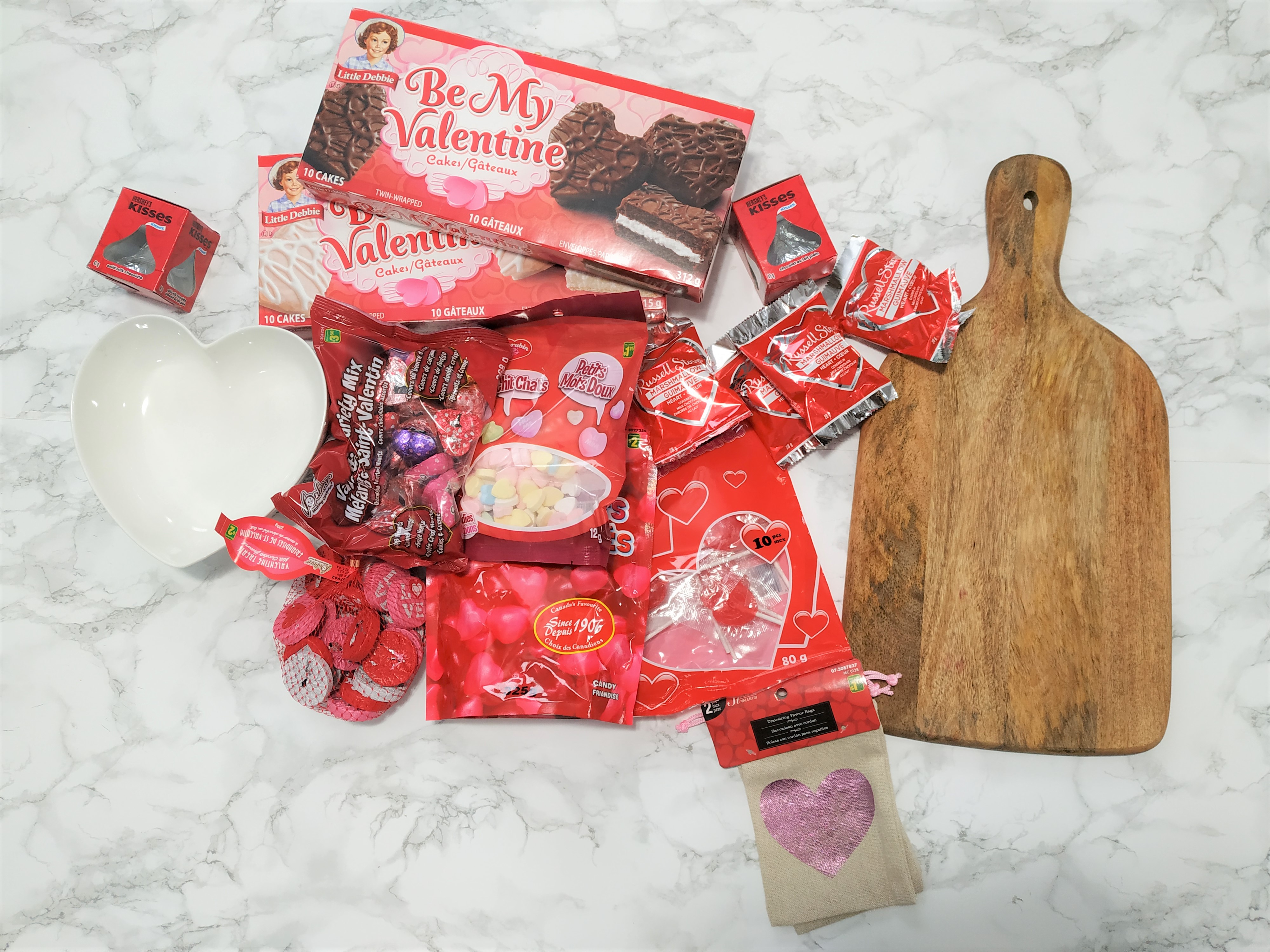 Packages of candy, a heart bowl and a charcuterie board on a table.