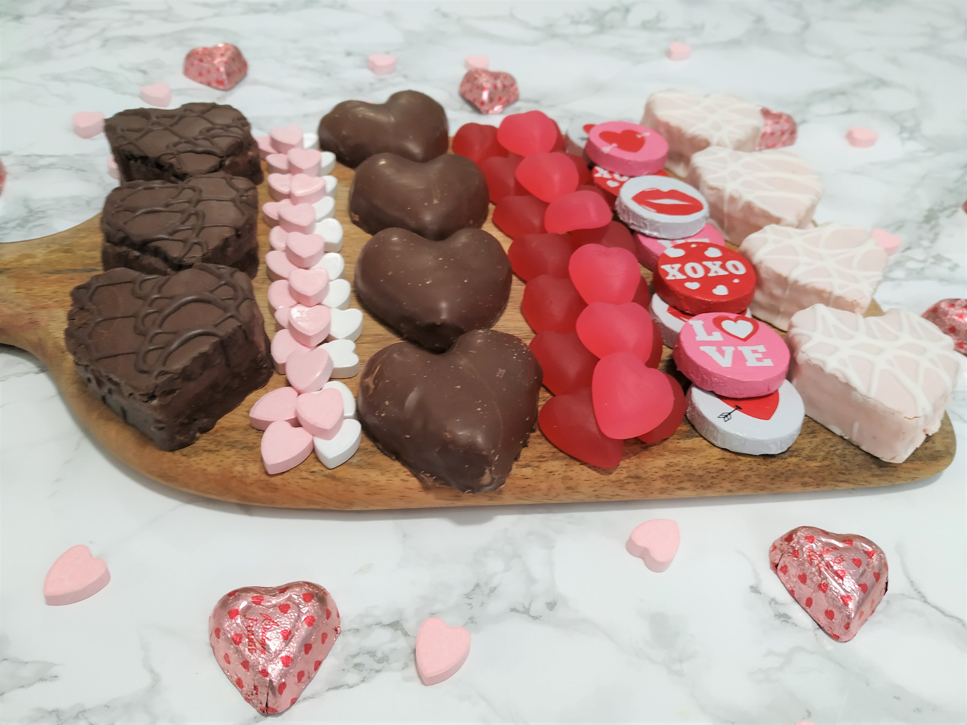 Candy, chocolates and cakes put on a charcuterie board with candy hearts sprinkled around.