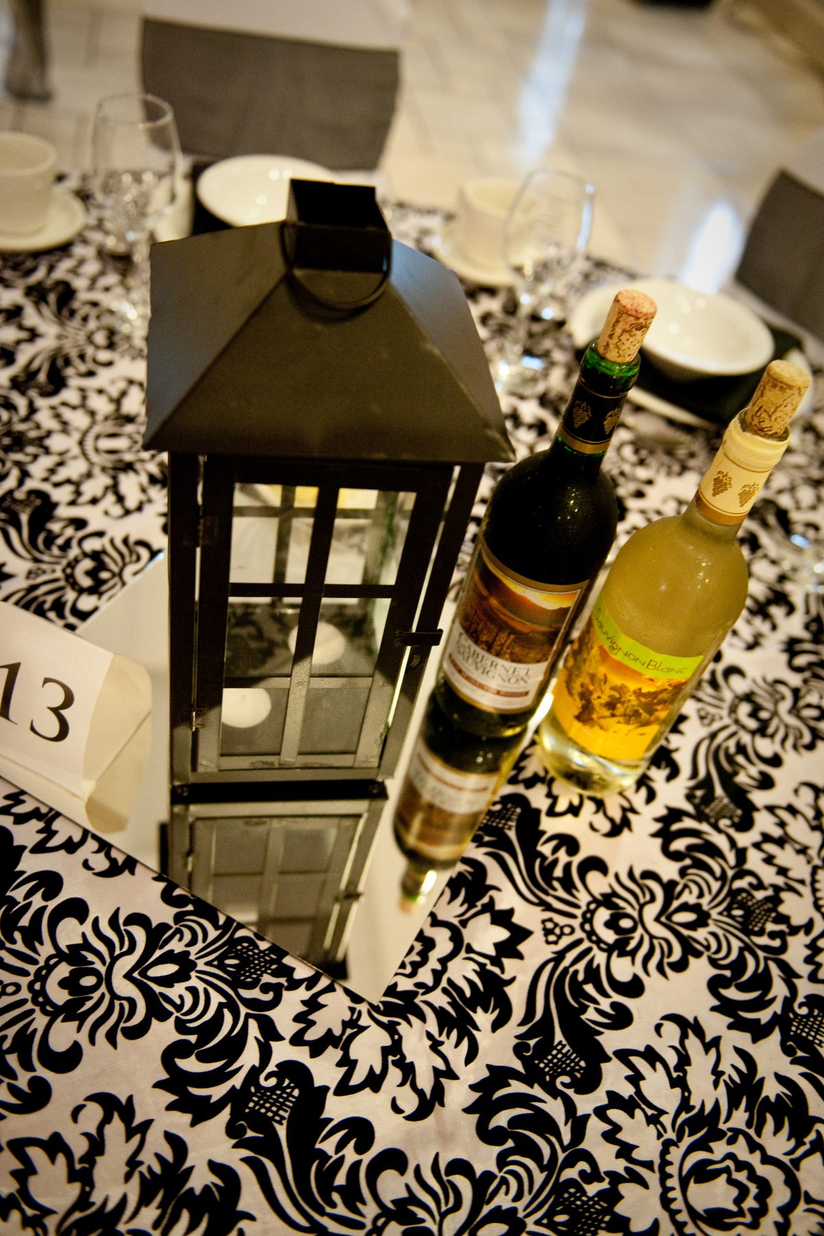 Black lantern wedding centerpiece next to bottles of wine.