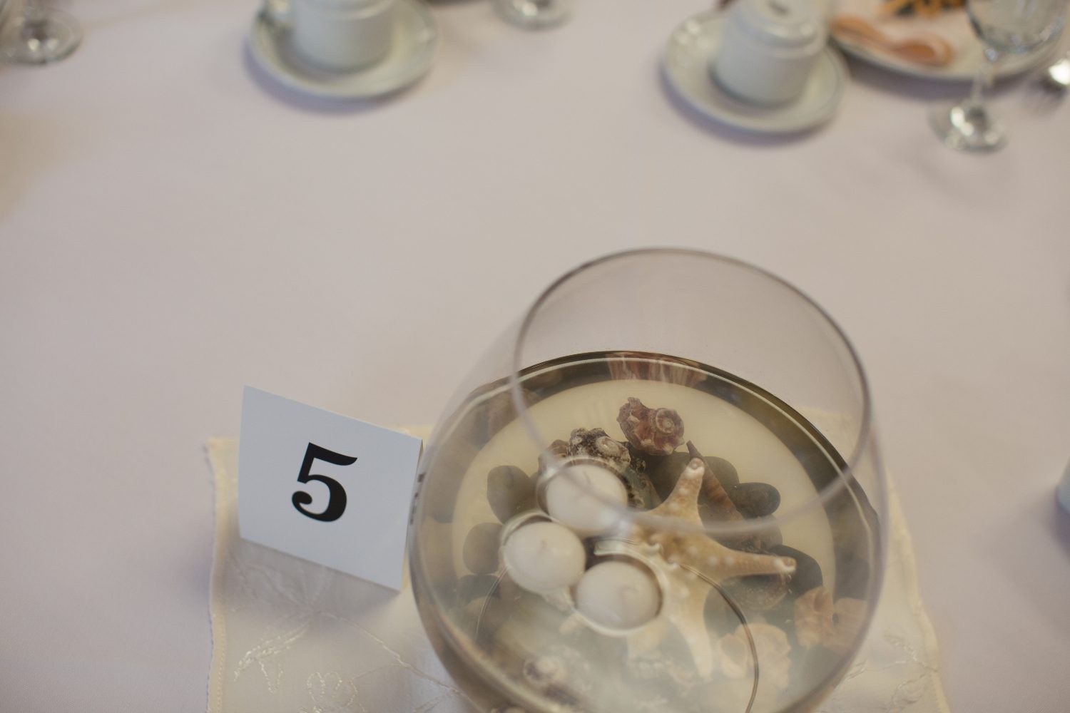 Fish bowl with candles, rocks and starfish on a table.