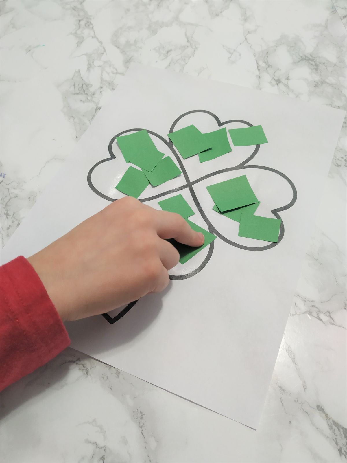 Gluing green paper shapes onto the shamrock coloring page.