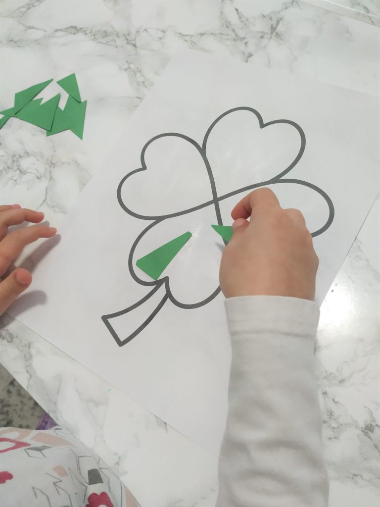 Gluing green paper shapes onto the shamrock coloring page.