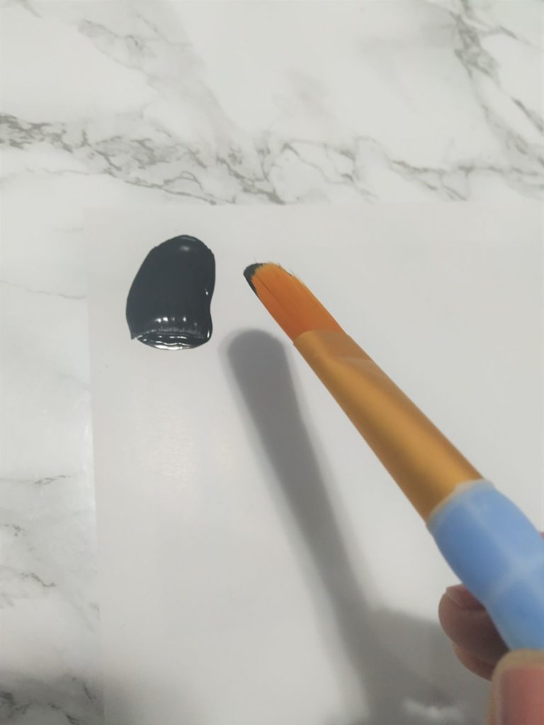Adding a brush stroke of black paint onto a piece of paper.