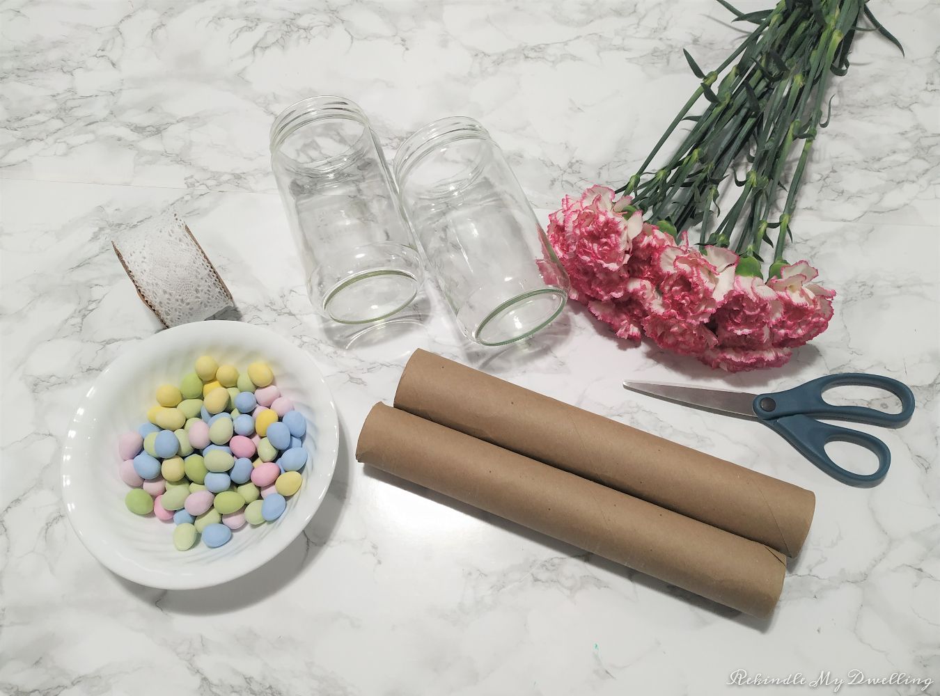 Materials to make Easter candy jars including candy, mason jars, ribbon, scissors, flowers and cardboard tubes.