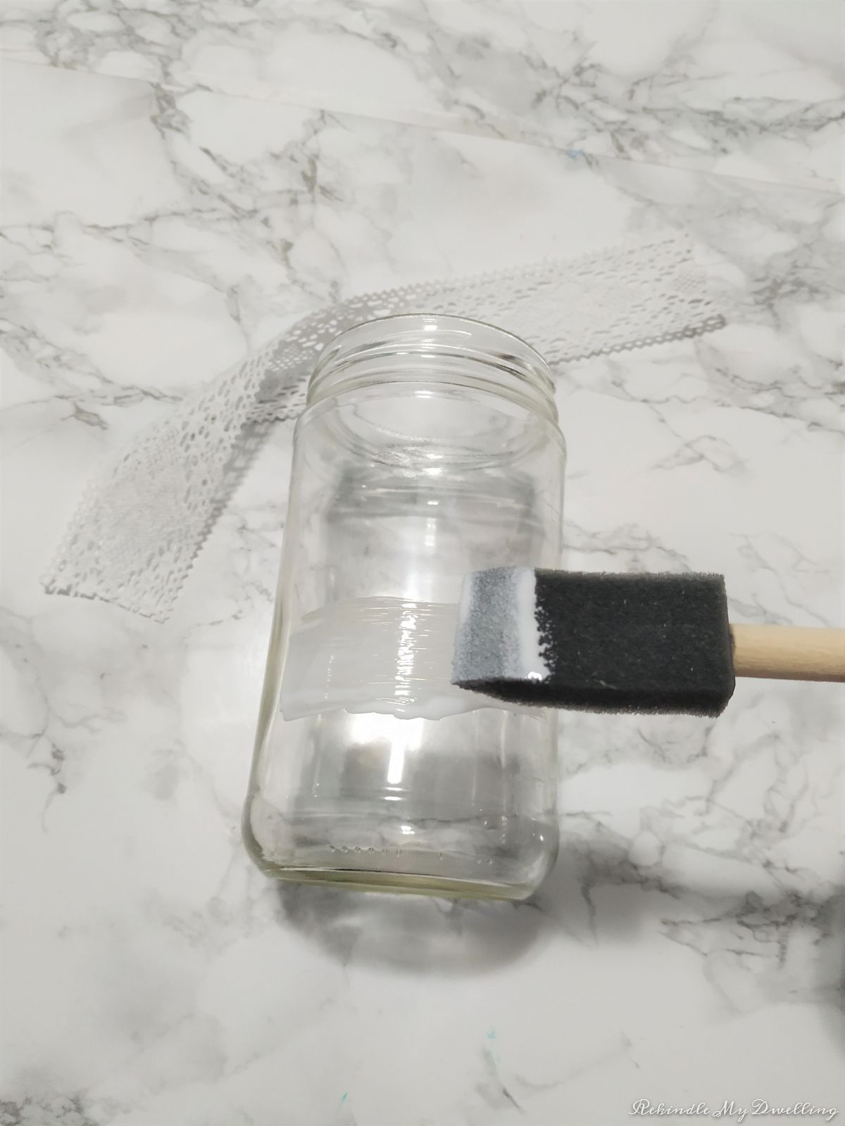Using a paint brush to add Mod Podge around the mason jar.