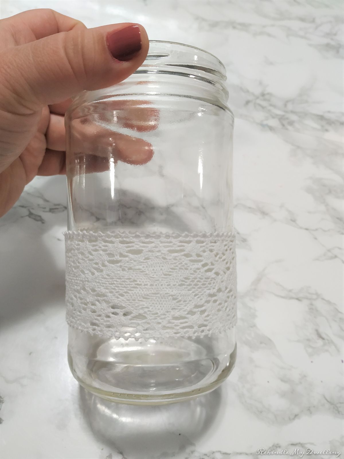 A hand holding a mason jar tied with lace fabric.