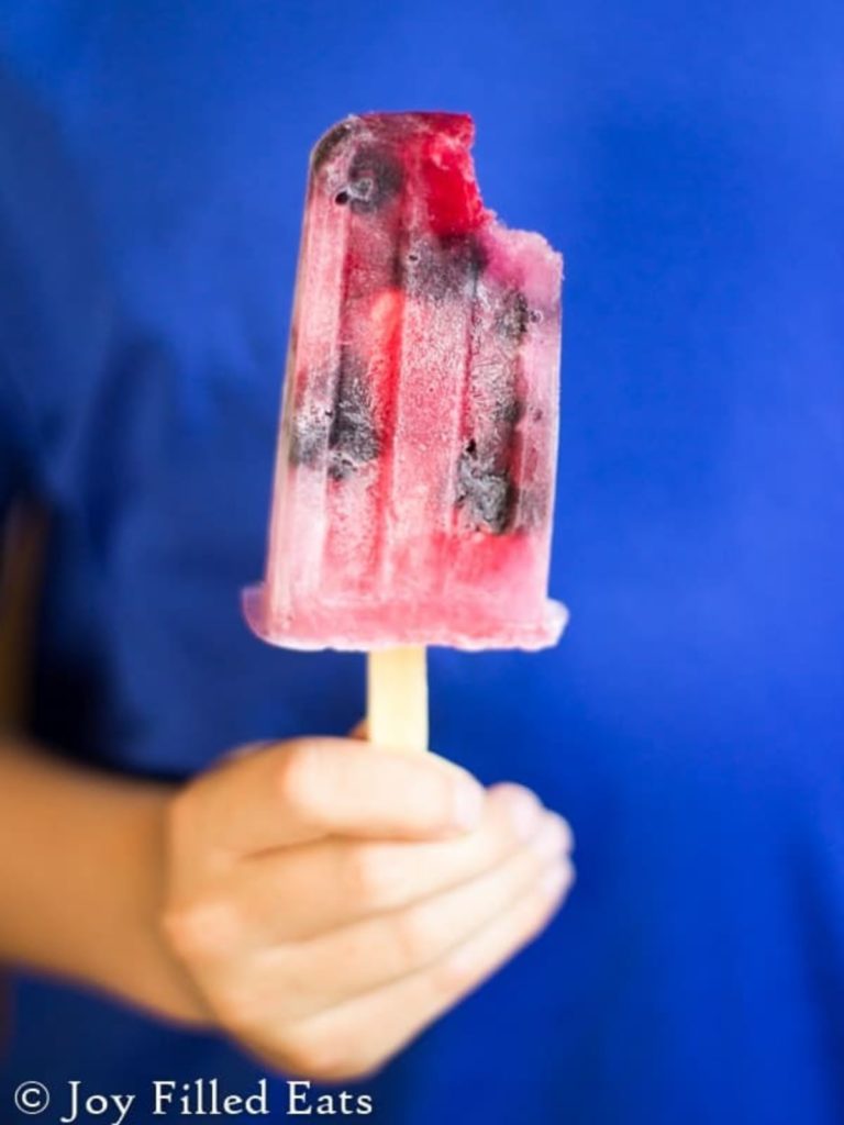 A hand holding a popsicle with a bite taken out.