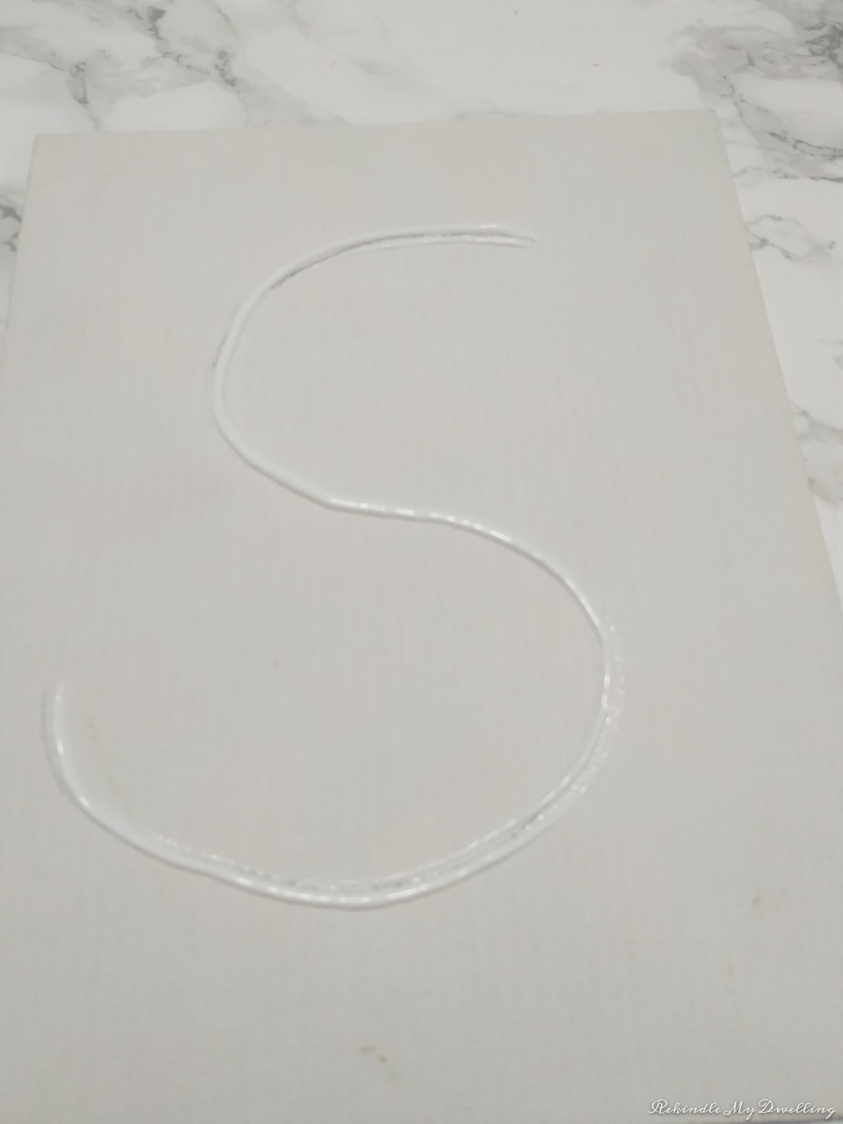 Adding glue to the lines letter S on the canvas.
