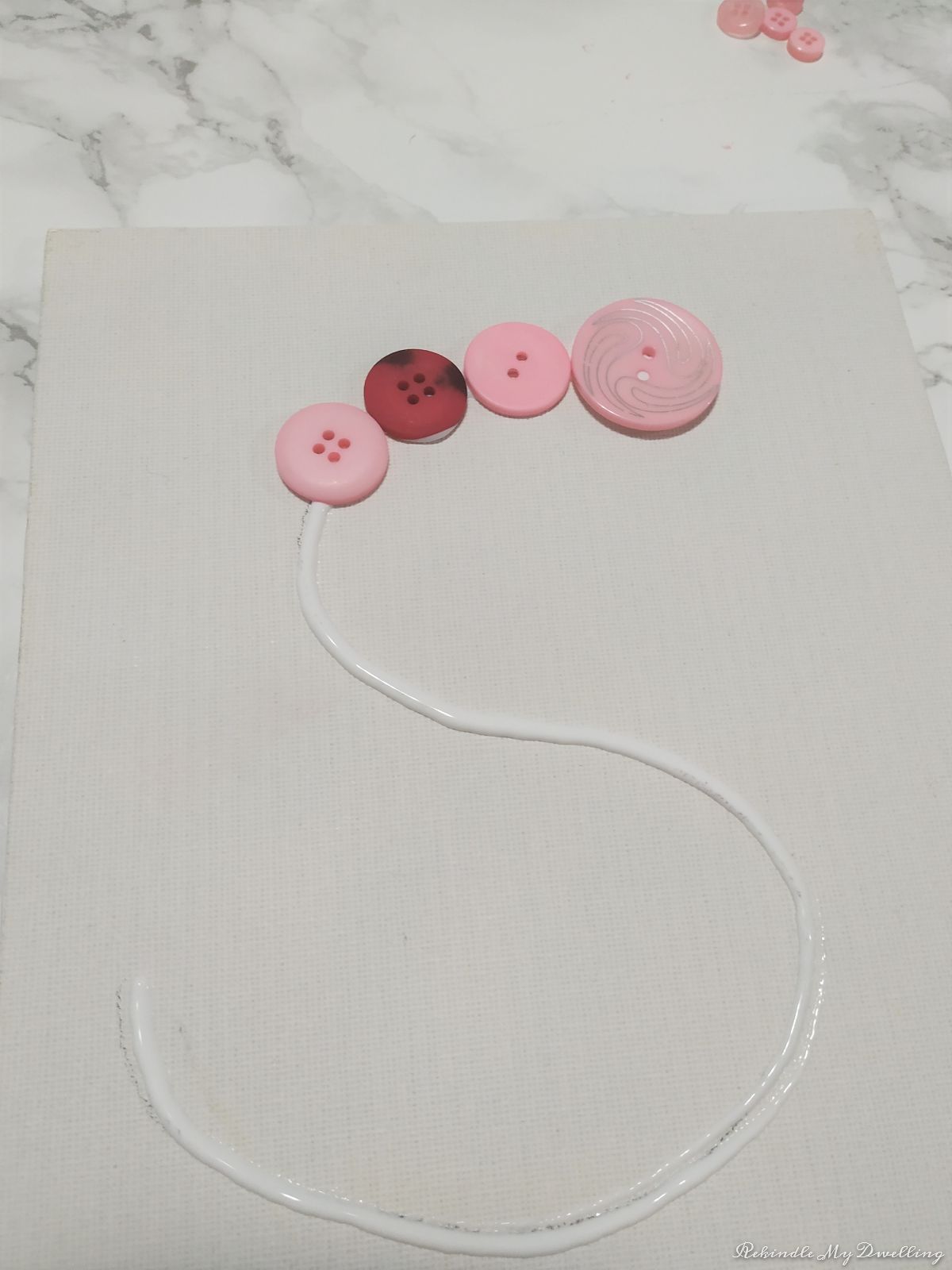 Gluing pink buttons to the canvas.