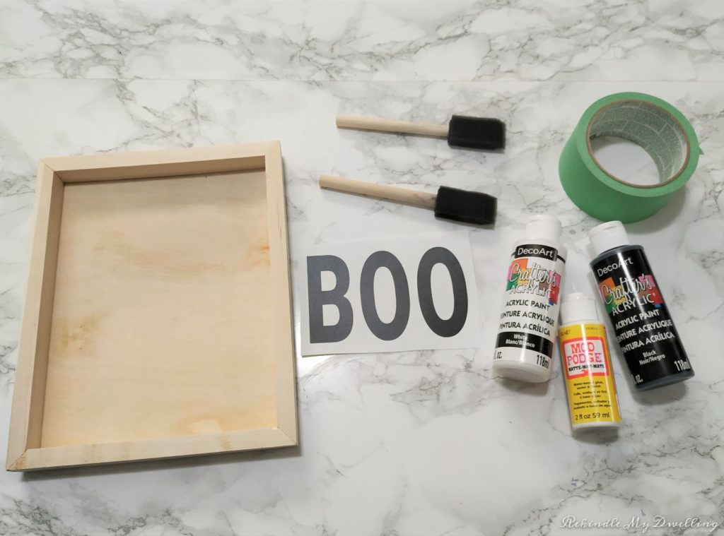 Materials needed to make a halloween wood tray, including a canvas piece, paint, tape, paint brushes and wording.