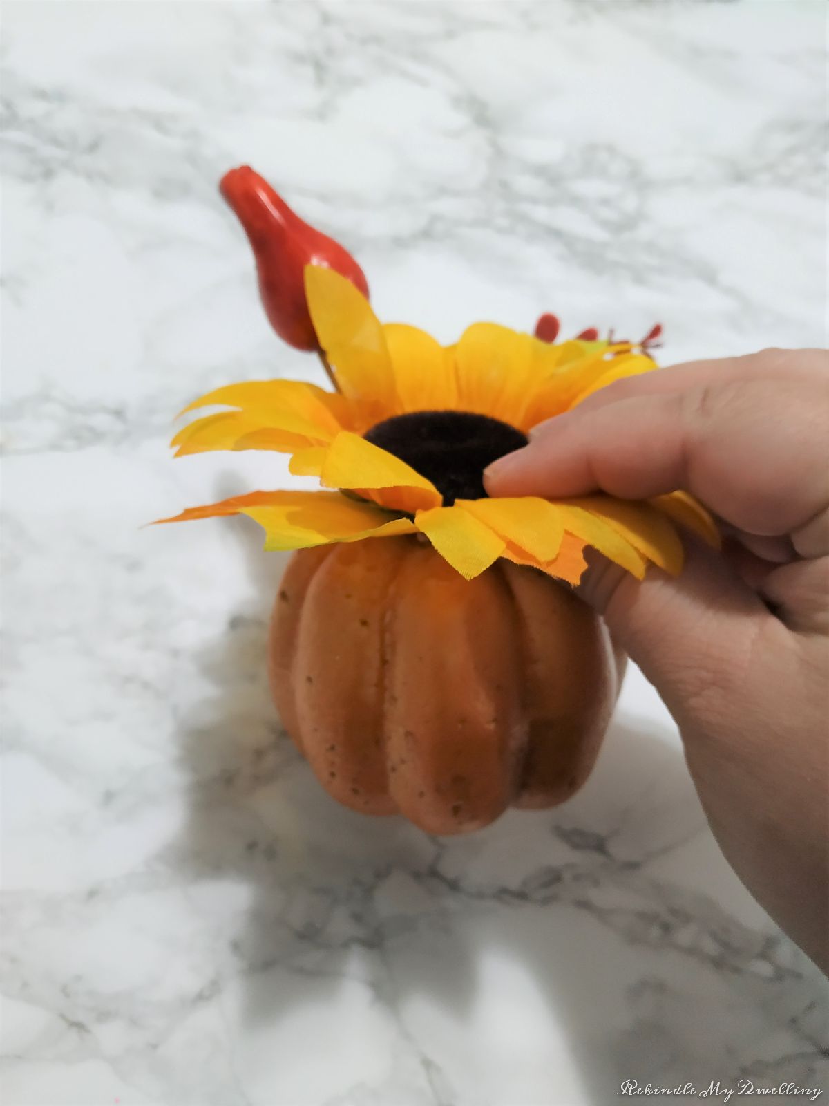 Removing faux flowers from a foam pumpkin.