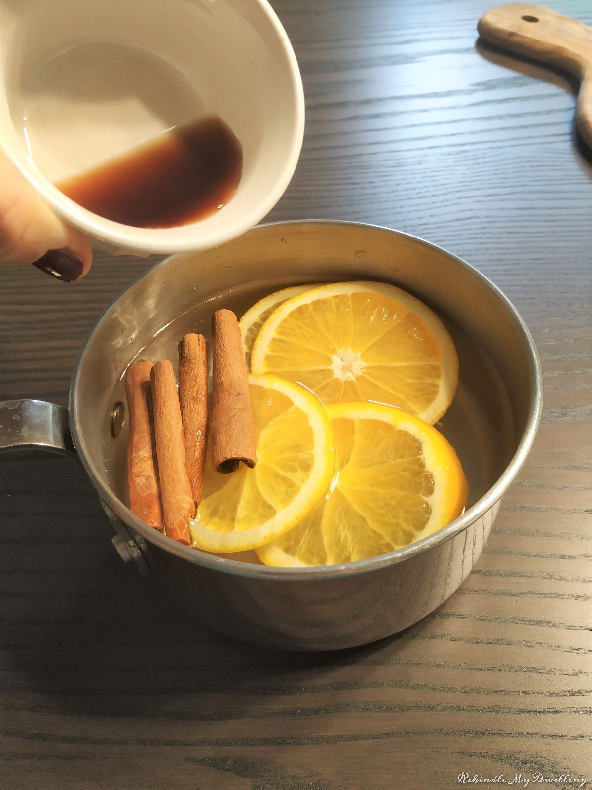 Adding vanilla extract into a pot water alongside orange slices and cinnamon sticks.