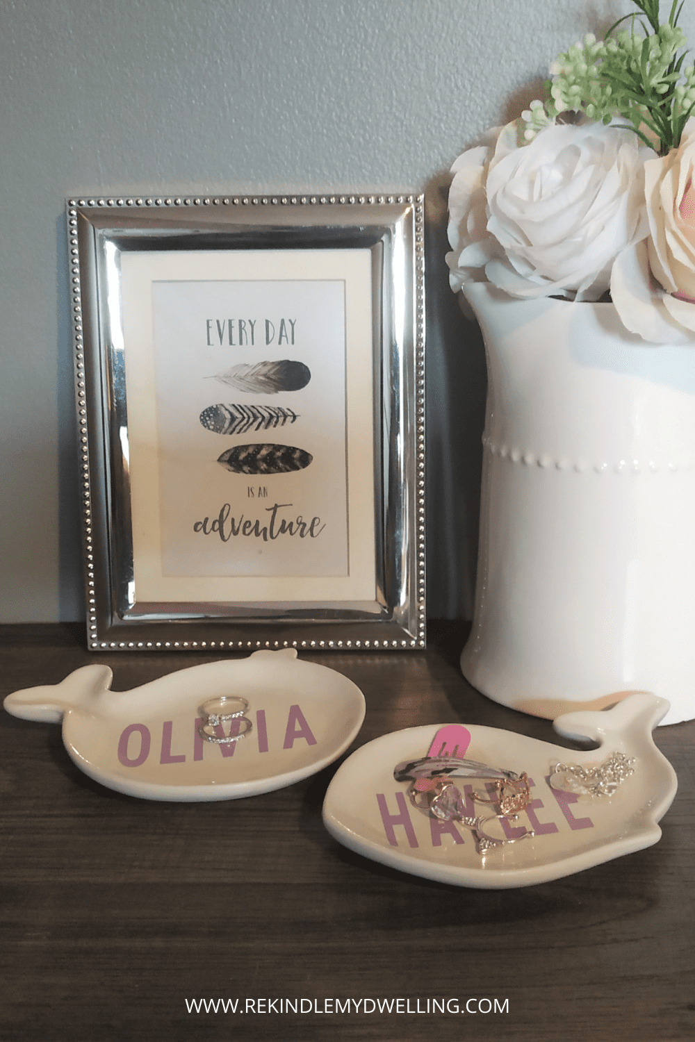 Personalized trinket dishes next to a vase with flowers and a picture frame.