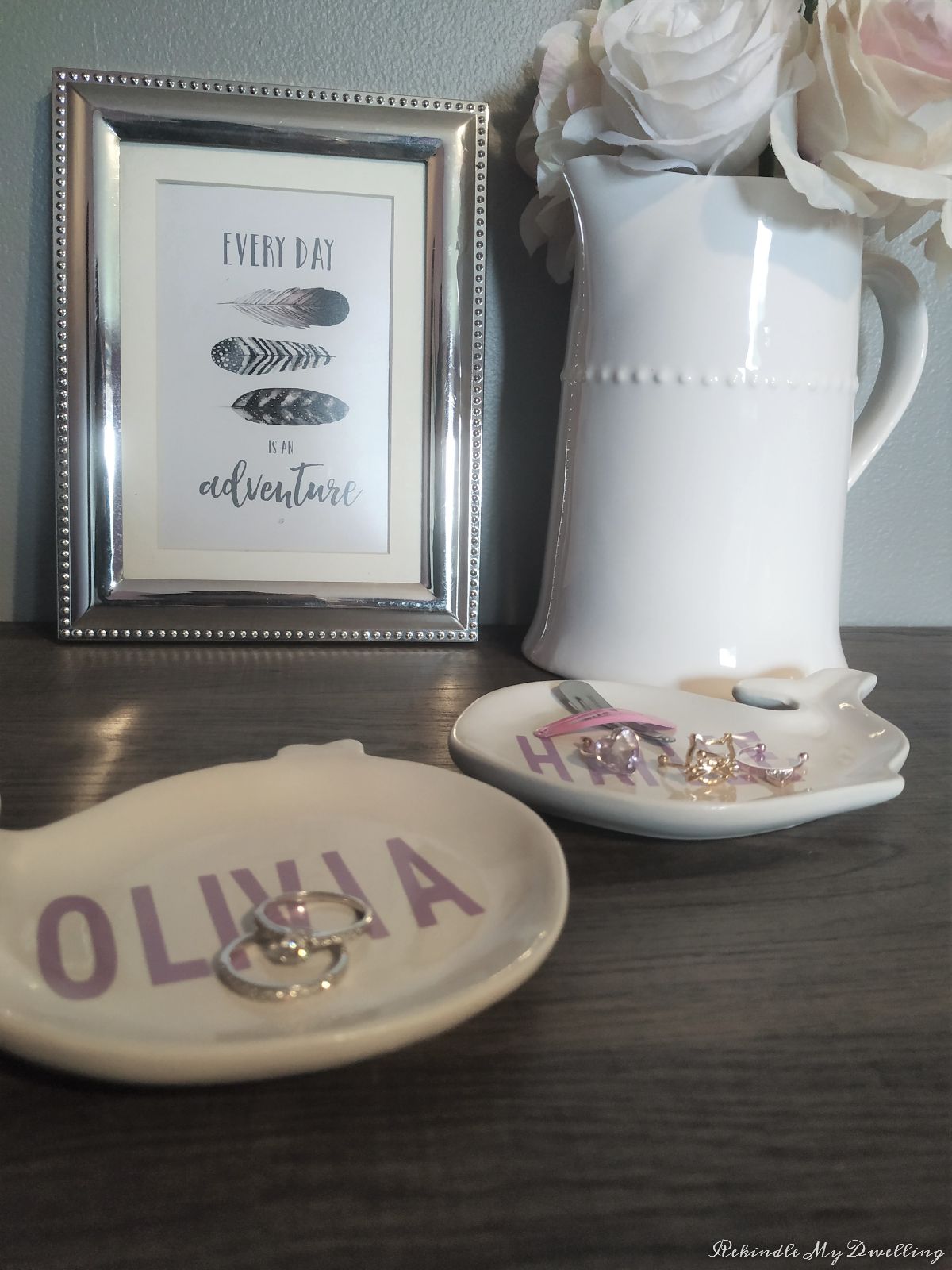 Personalized trinket dishes next to a vase with flowers and a pciture frame.