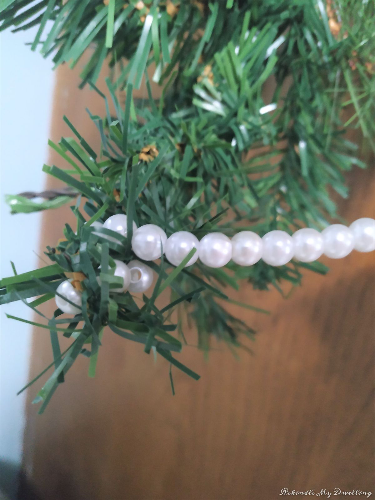 Wrapping pearl garland around a pine garland.