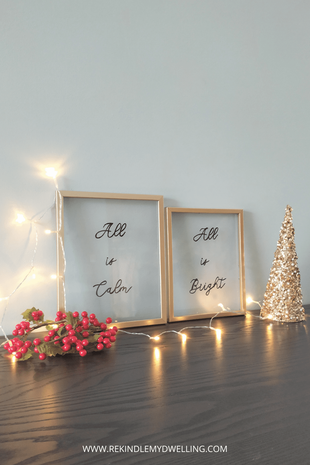 Framed glass floating signs next to lights, holly and a mini Christmas tree.