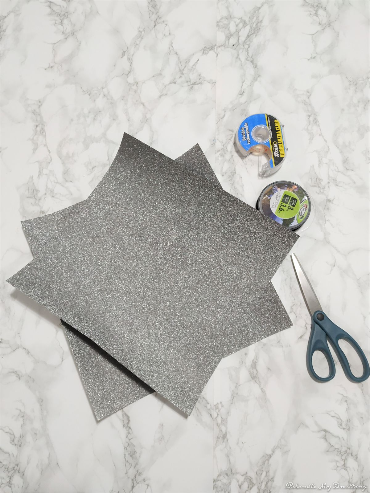 Materials needed to make paper star ornaments including scrap paper, tape, fishing wire and scissors. 