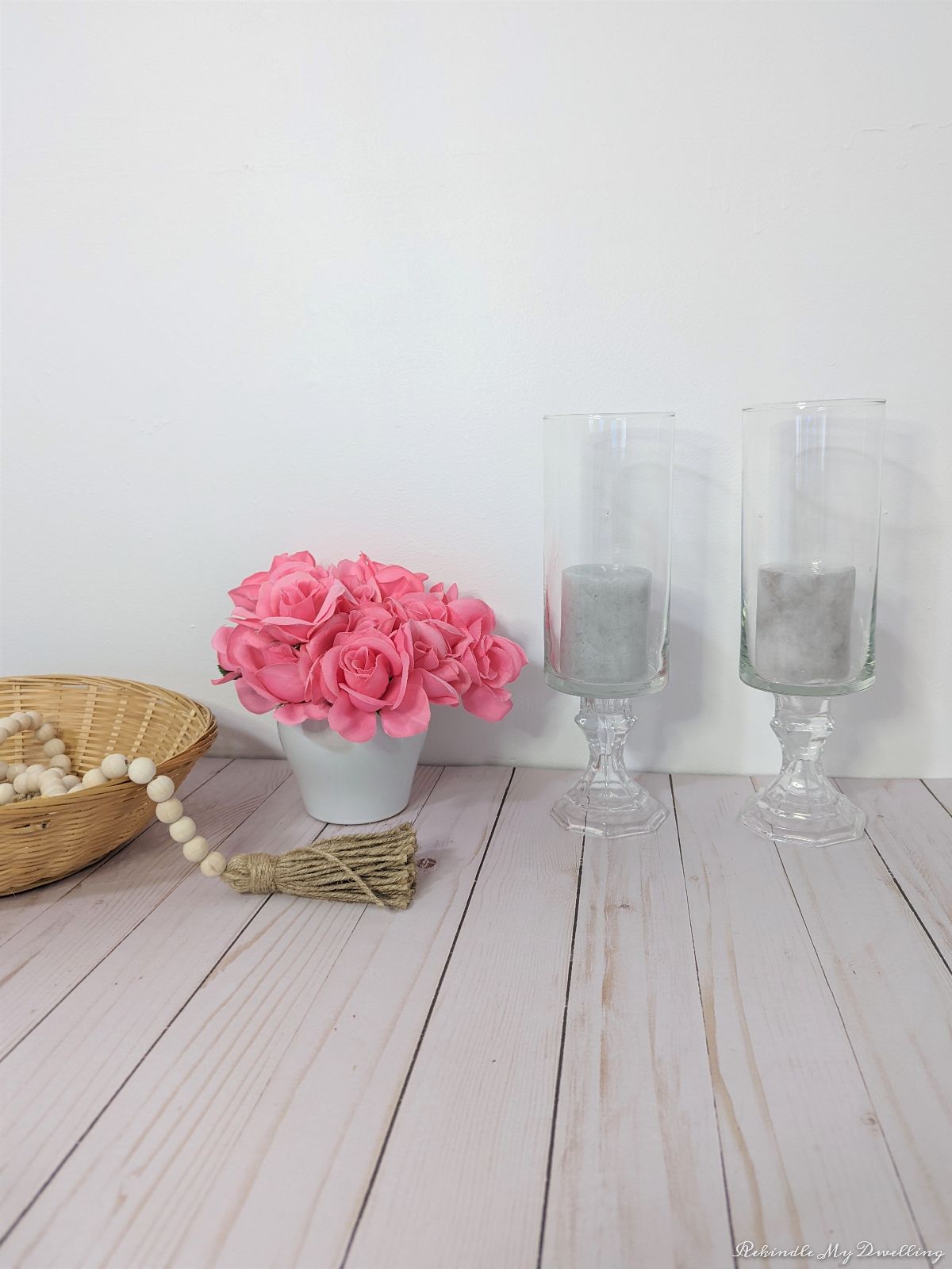 Pedestal vases with candles next to a bouquet of flowers, basket and garland.