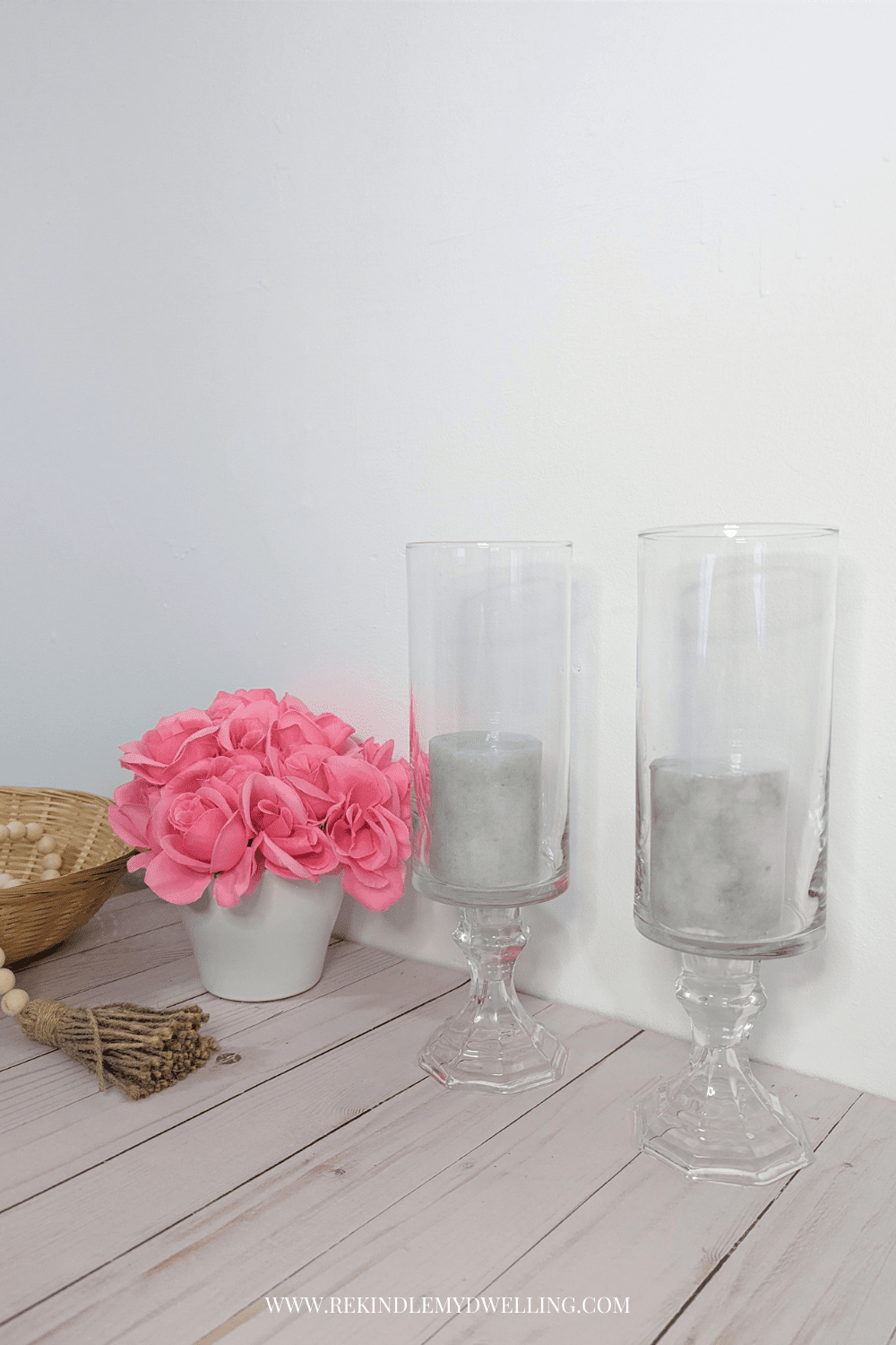 Pedestal vases with candles placed next to a bouquet of flowers and beads.