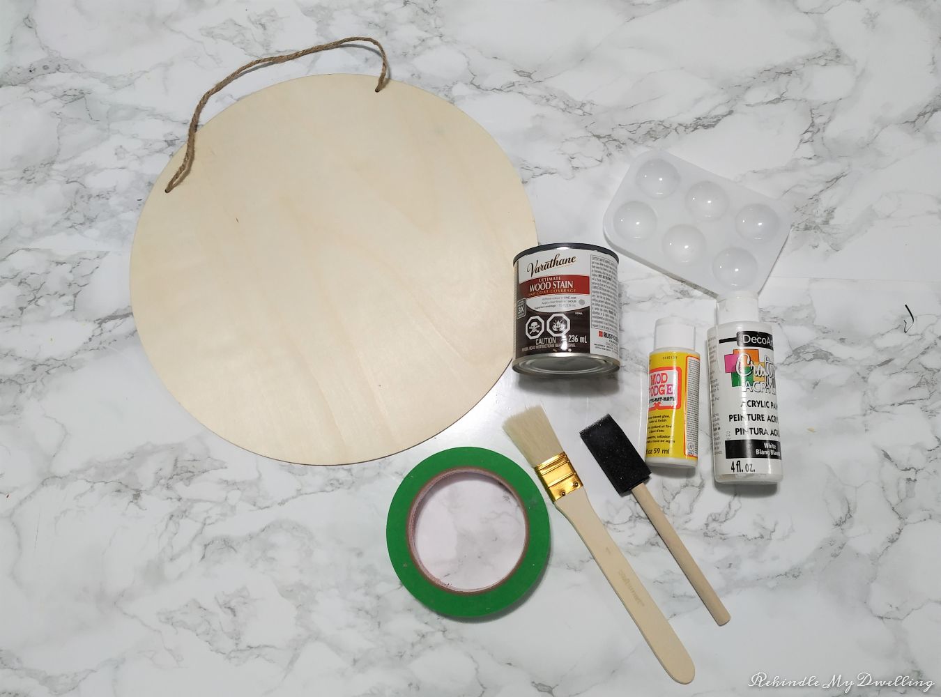 Materials needed to make a diy wood sign including a wood circle, paint, paint brushes, and tape.