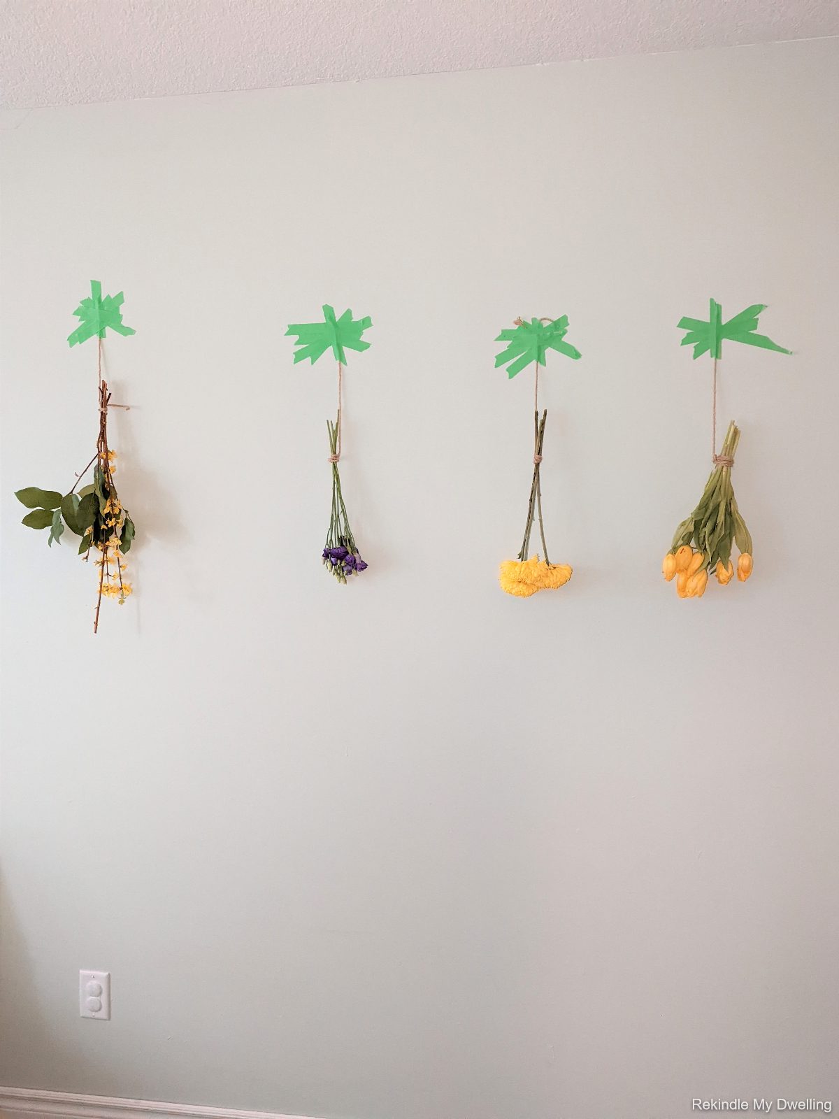 Flowers tied together and hung on a wall upside down.