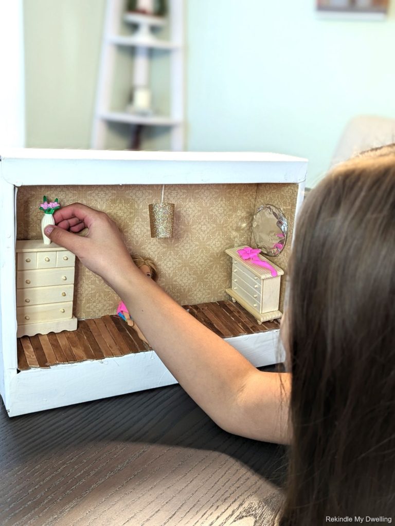Girl playing with a doll in a diy cardboard box dollhouse.