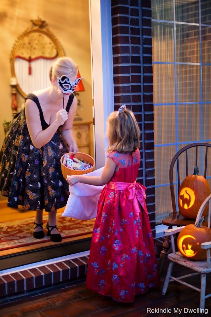 Masked woman handing out candy to a child.