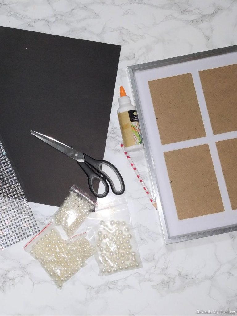 Materials needed to make a diy moon decor, including paper, pearls, picture frame, scissors and glue.