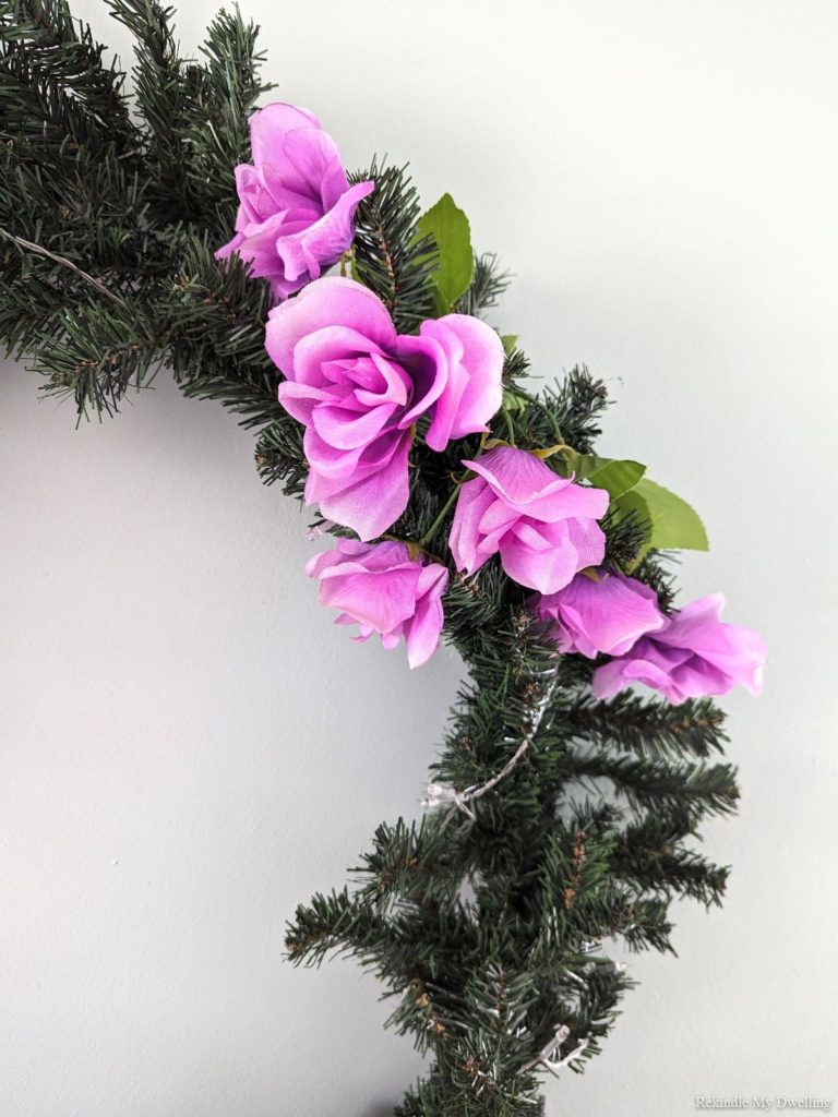 Placing faux flowers around an evergreen wreath.
