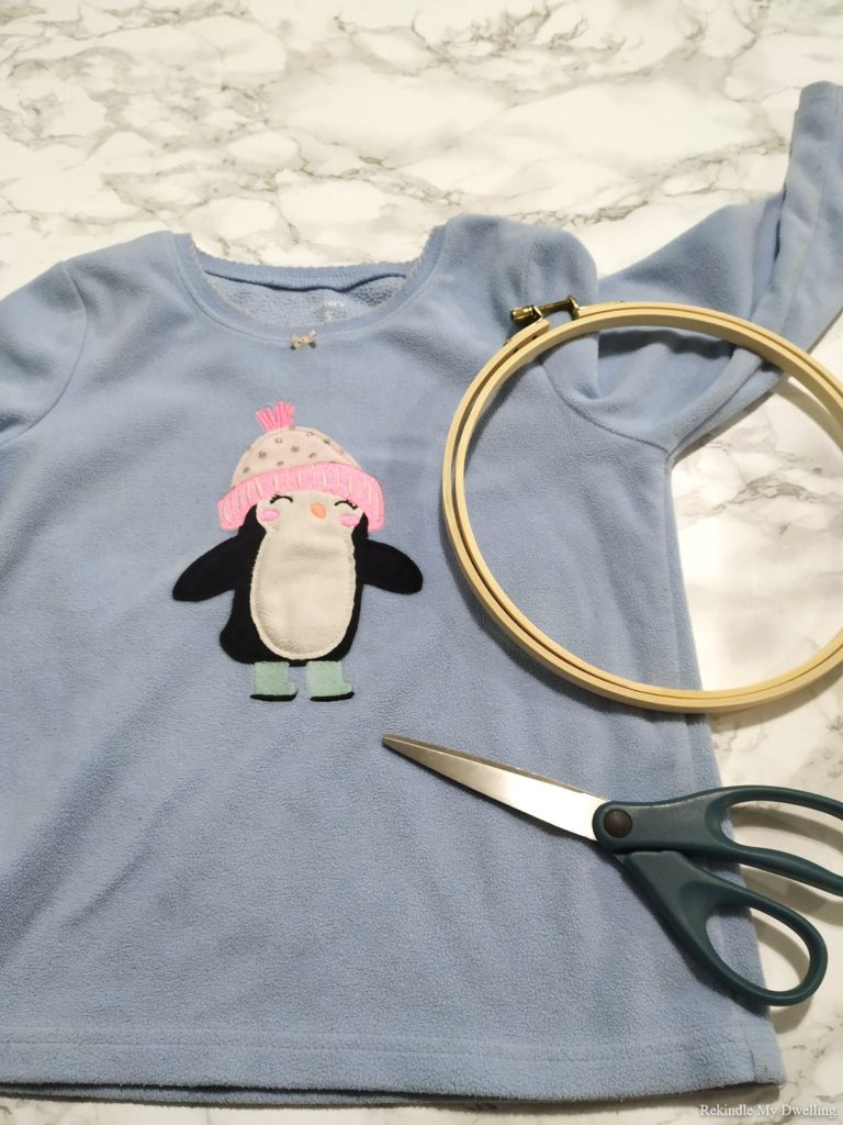 Materials needed to make an upcycled wall art including a sweater, hoop and scissors.