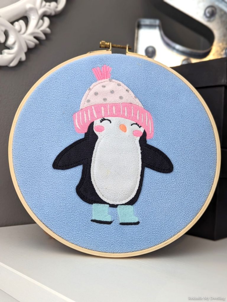 Upcycled wall art with an embroidery hoop and penguin sweater.