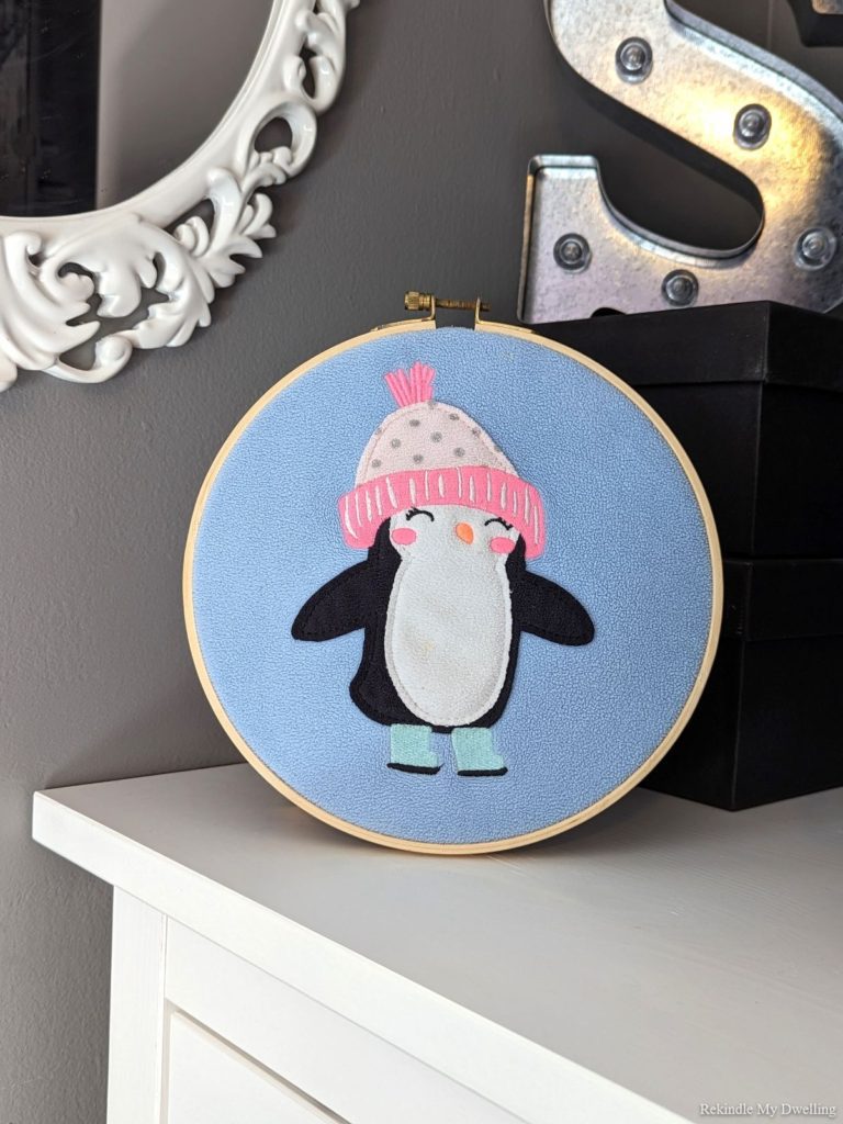 Upcycled wall art with an embroidery hoop and penguin sweater.