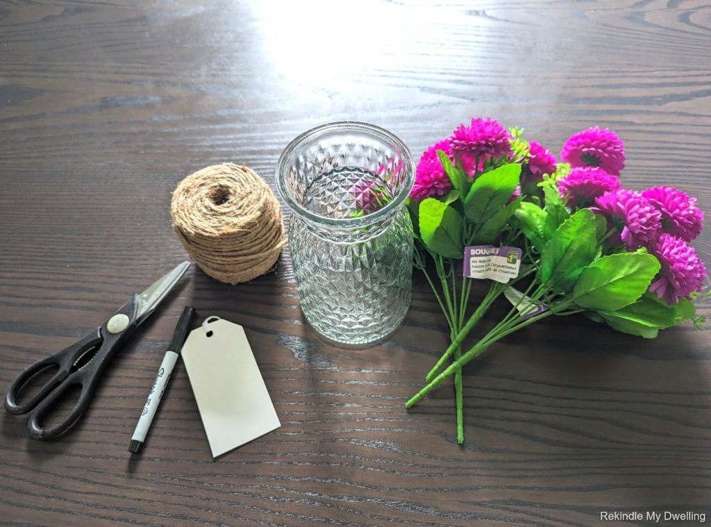 Materials needed to make a nice housewarming gift including a vase, faux flowers and twine.