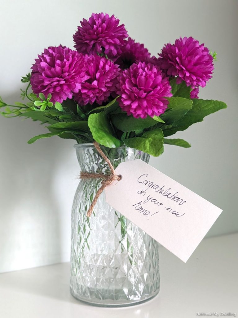 Nice housewarming gift idea of a vase filled with purple flowers and wrapped with ribbon.