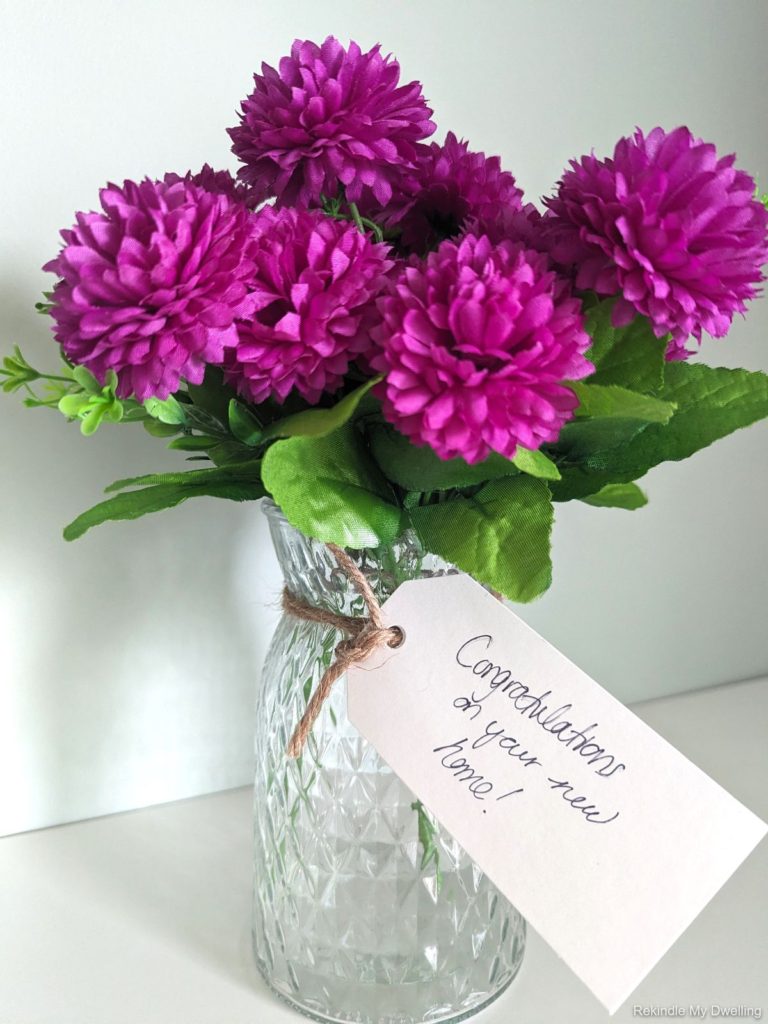 Nice housewarming gift idea of a vase filled with purple flowers and wrapped with ribbon.